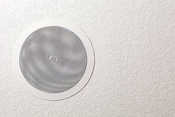 White wall-mounted speaker on a brown column beneath a tiled ceiling