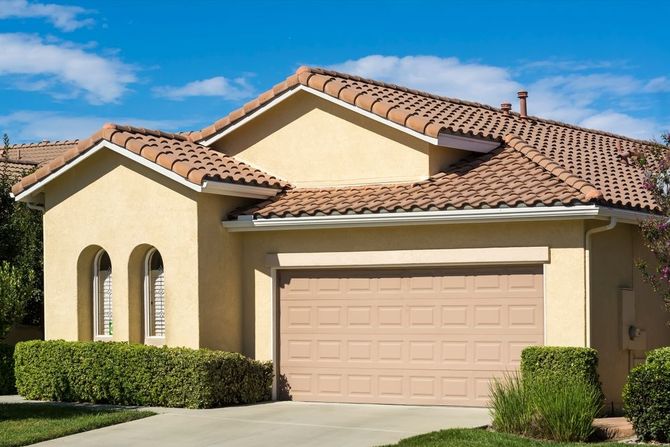 Suburban house with beige stucco, terracotta roof, and a two-car garage under a clear blue sky