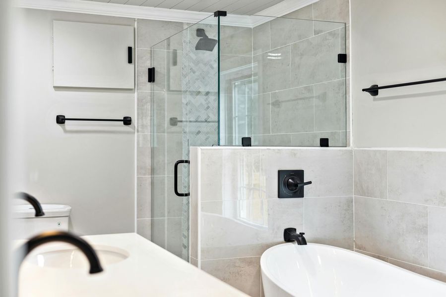 Modern bathroom with glass shower, white tub, and black fixtures.