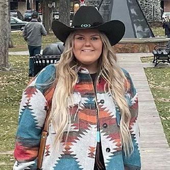 a woman wearing a cowboy hat and a colorful jacket is standing on a sidewalk .