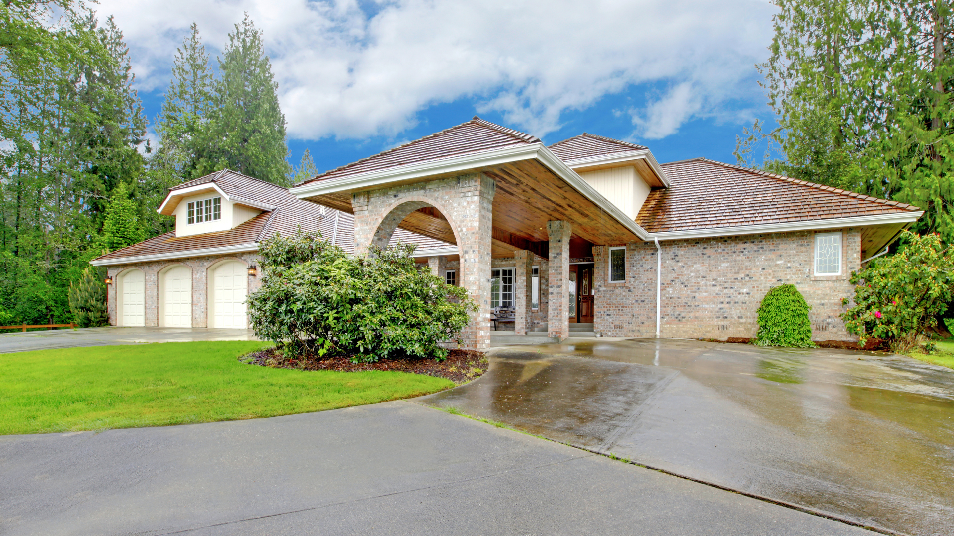 Large stone house with a covered entrance, arched columns, and a long driveway, surrounded by trees.