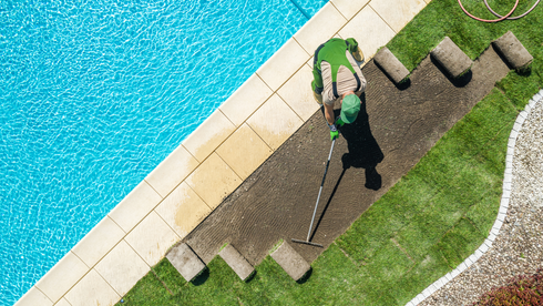 Person laying sod by a pool, green grass and rolls on a sunny day.