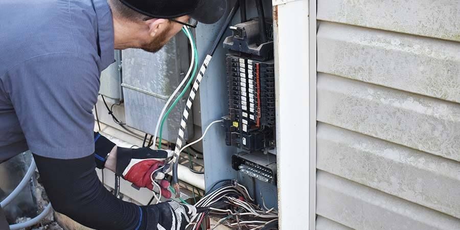 A man wearing a hard hat and gloves is working on an electrical box.
