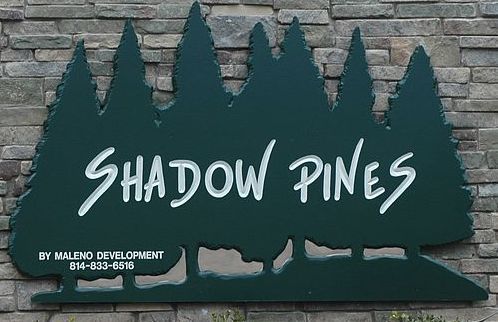 A sign for shadow pines is on a brick wall