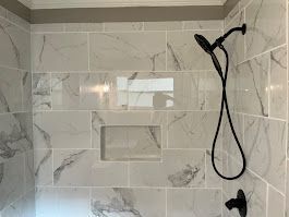 Shower with gray and white marble-look tiles, a recessed shelf, and black shower fixtures.