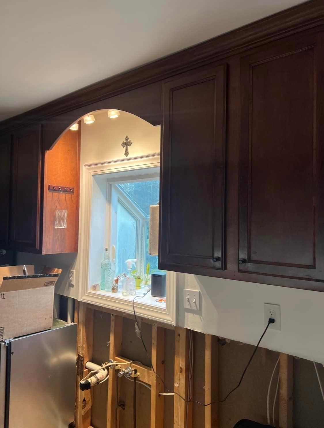 A kitchen with wooden cabinets and a window with a cross on it.