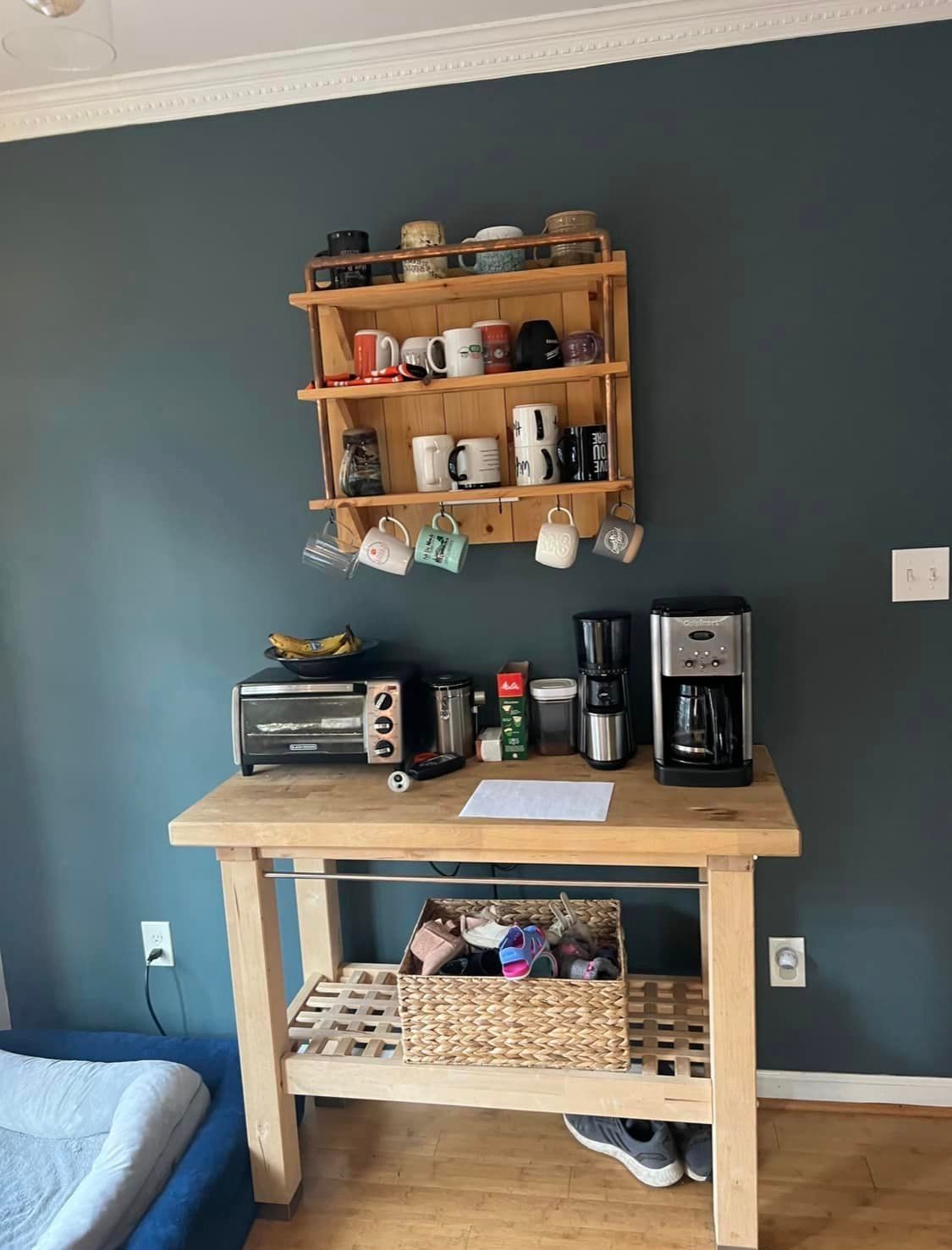 A coffee station with a wooden table , coffee maker , toaster oven , and mug rack.