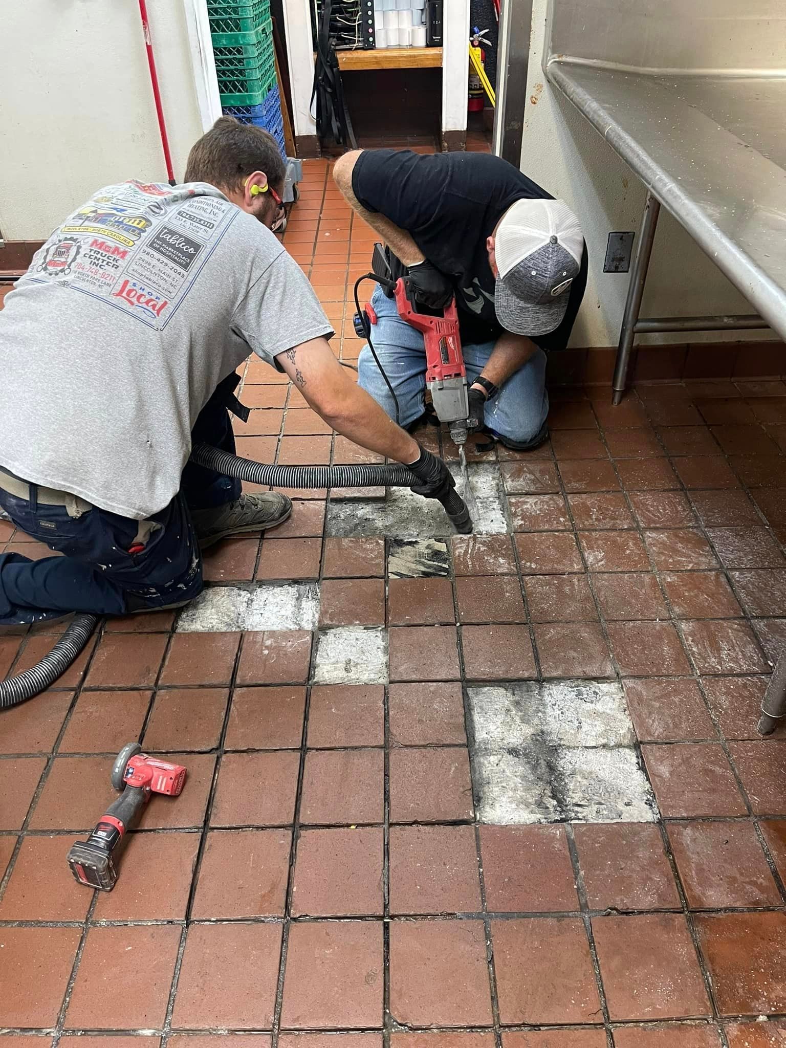 Two men are working on a tiled floor in a kitchen.