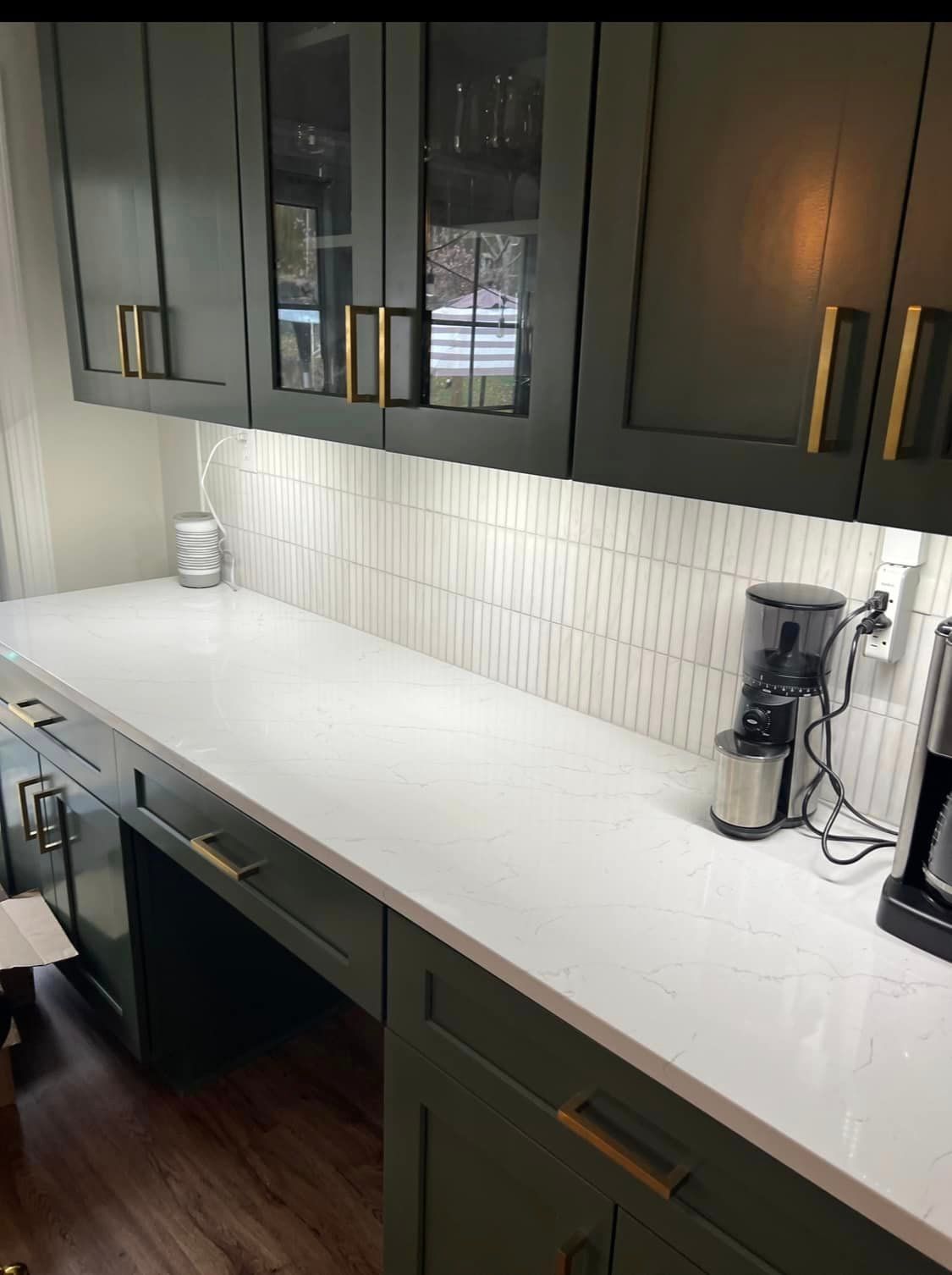 A kitchen with green cabinets , white counter tops , and a coffee maker.
