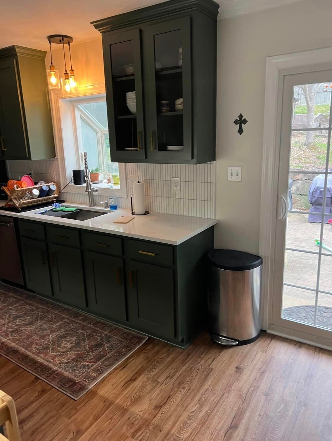 A kitchen with green cabinets and a stainless steel trash can.
