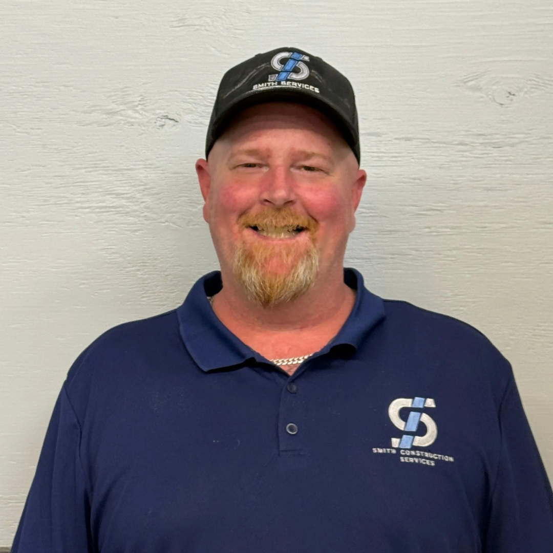 Man in blue polo and cap smiles at the camera, logo on shirt and hat.
