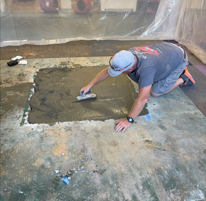 A man is kneeling on the floor using a trowel
