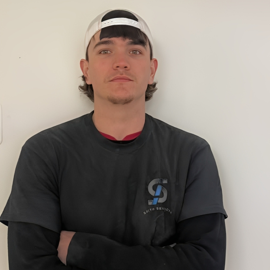 Man in blue polo shirt smiles in front of a green tree.