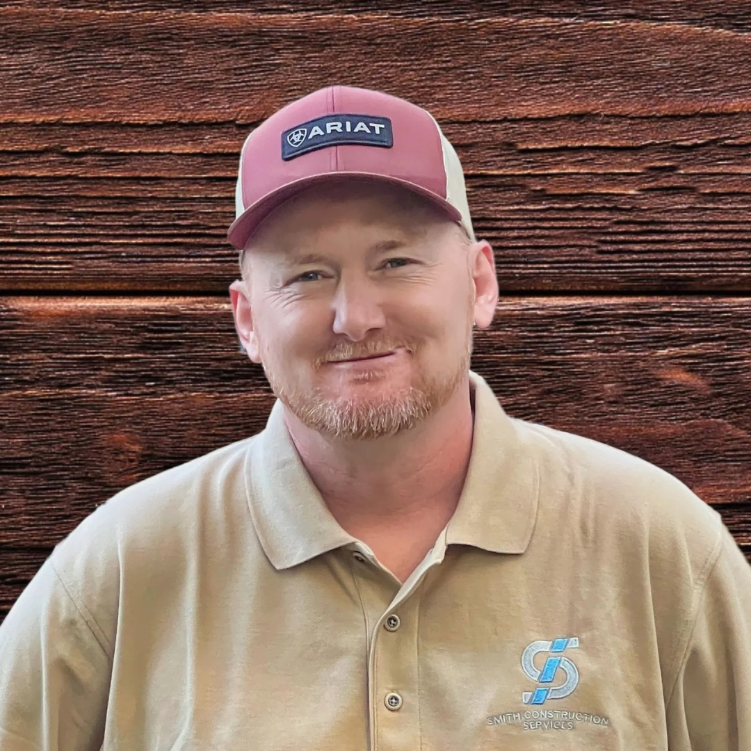 Man wearing a baseball cap and polo shirt, smiling in front of a wood background.