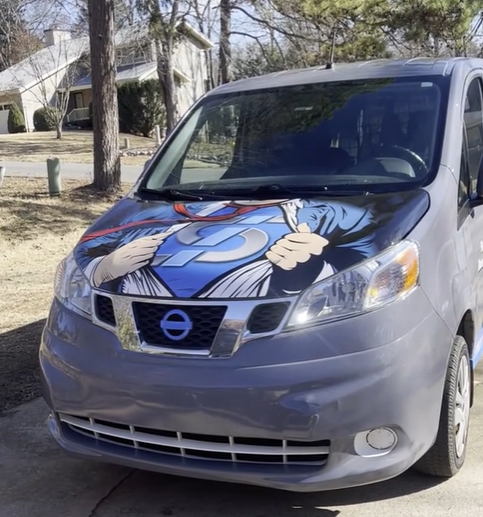A nissan van with a superman hood wrap