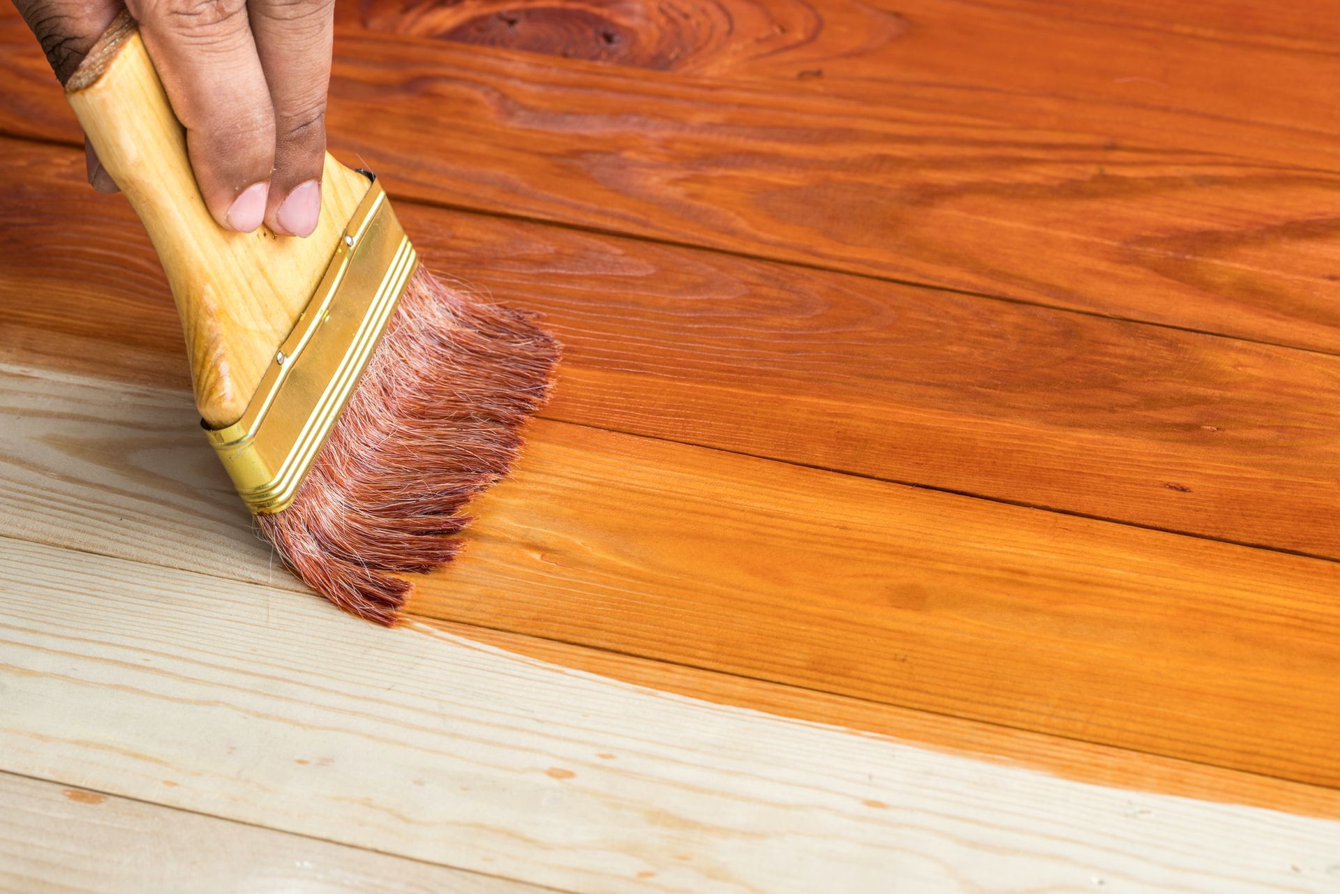 A person is painting a wooden floor with a brush.