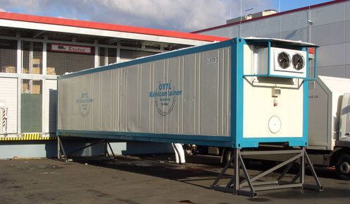 Ein blau-weißer Kühlcontainer von OTTL-CONTAINER steht vor einem Gebäude.