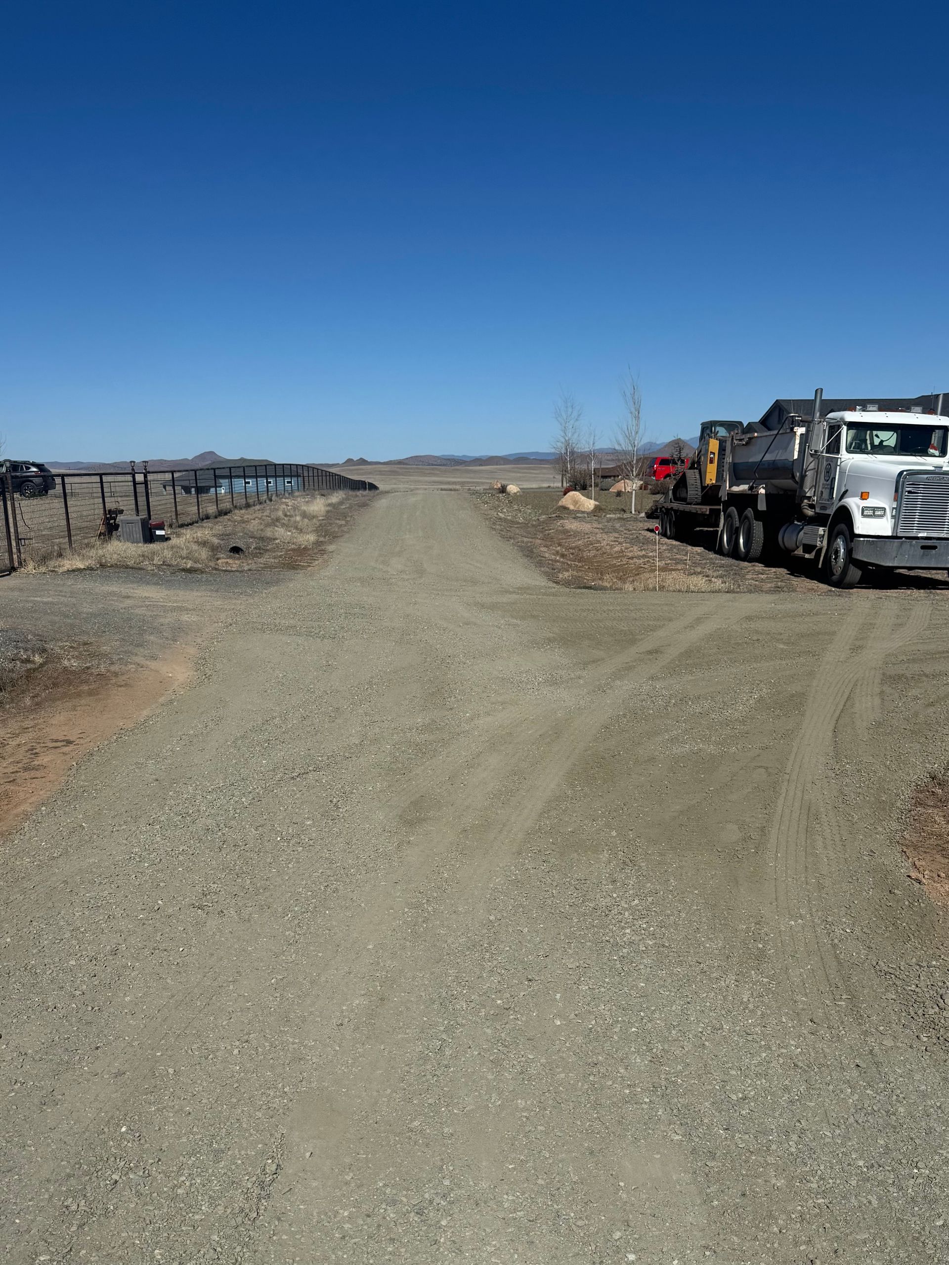 Gravel road in a rural area with parked utility trucks under a clear blue sky