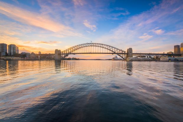 Il Sydney Harbour Bridge al tramonto, che si inarca sulle acque calme e sul cielo colorato.