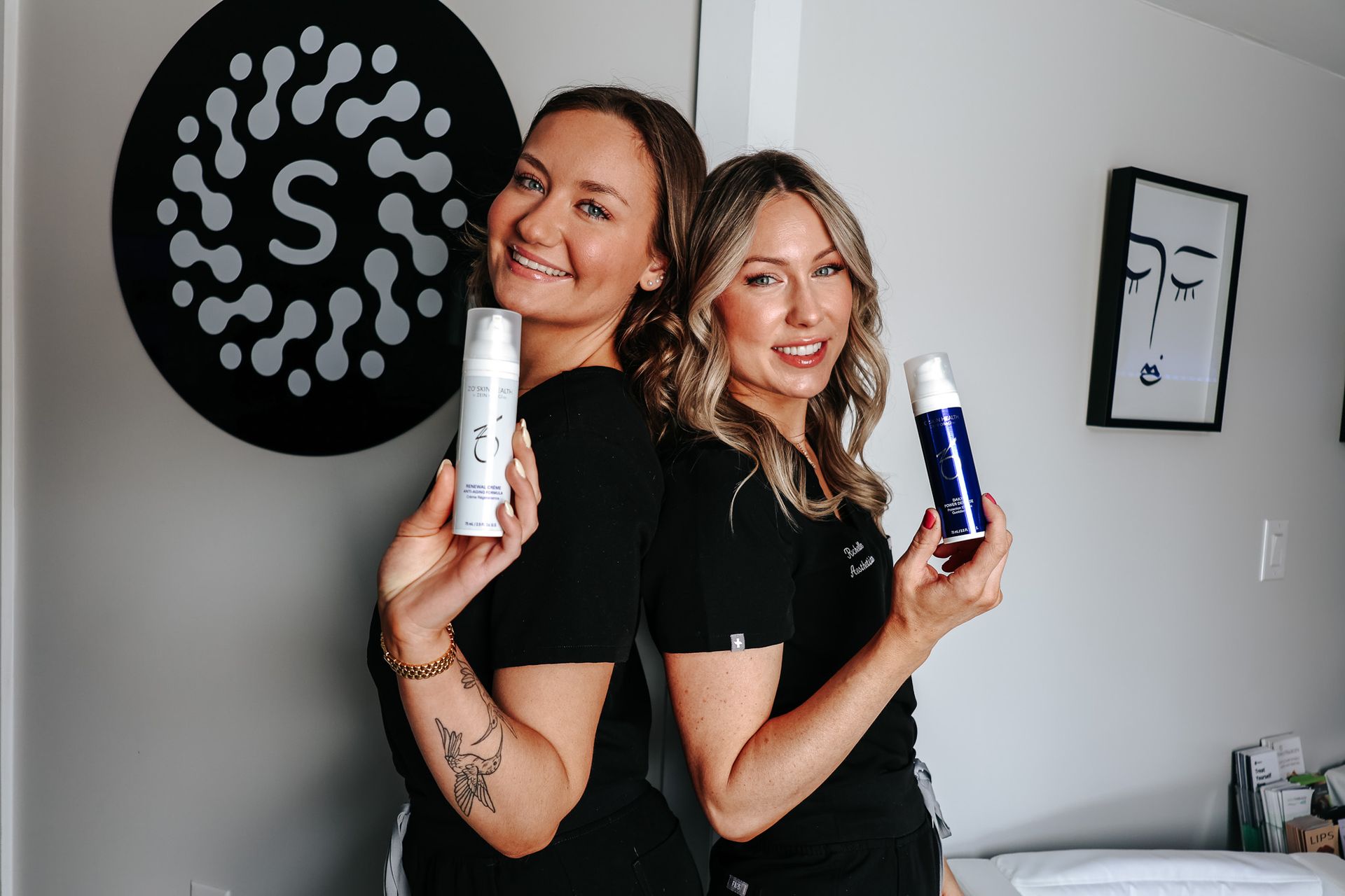 Two women are standing back to back holding bottles of cosmetics.