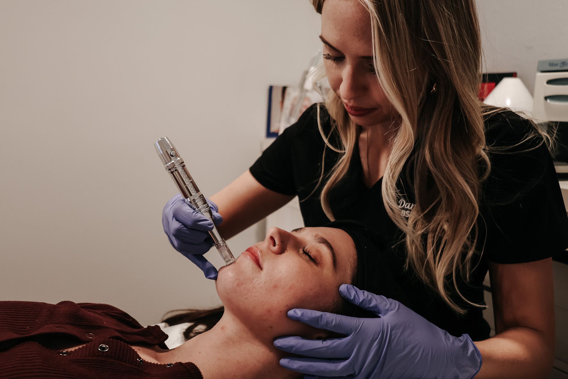 A woman is using a machine on a patient 's face.