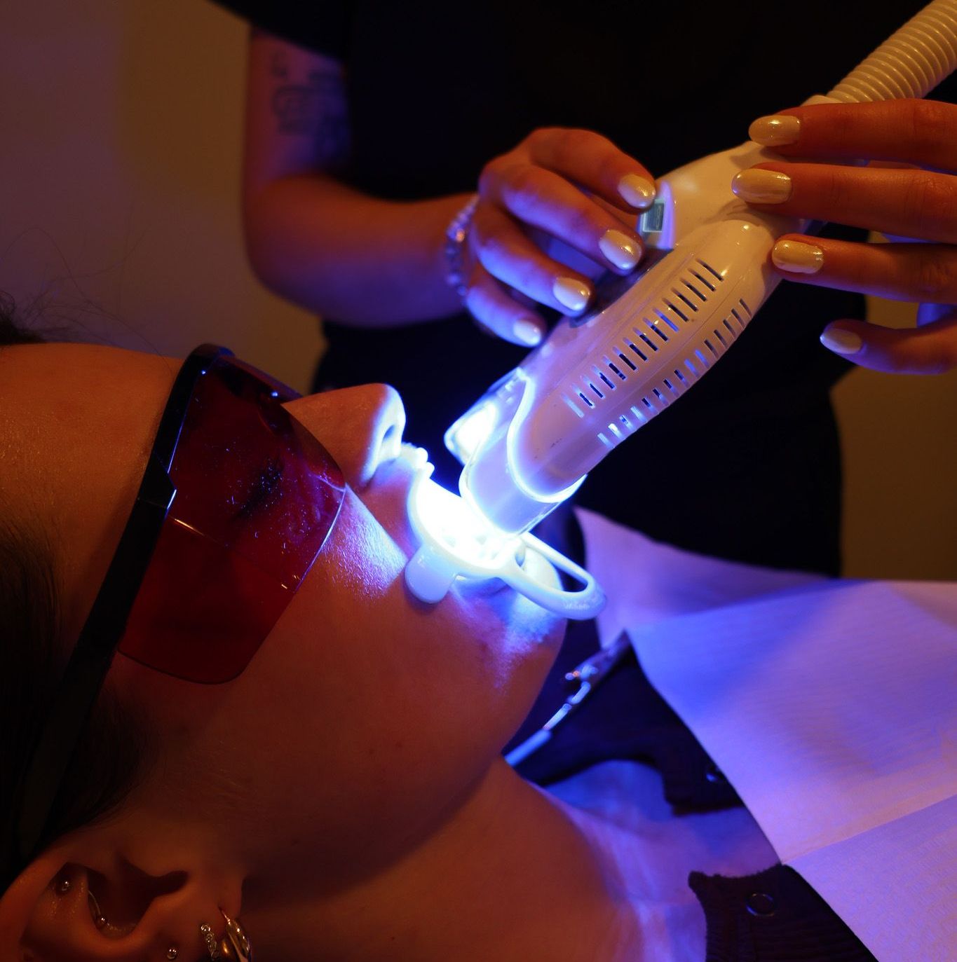 A woman wearing glasses is getting her teeth whitened
