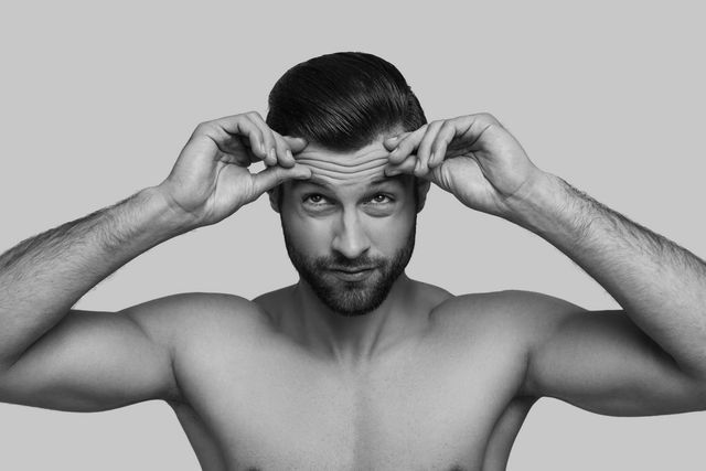 A shirtless man is touching his forehead with his hands in a black and white photo.