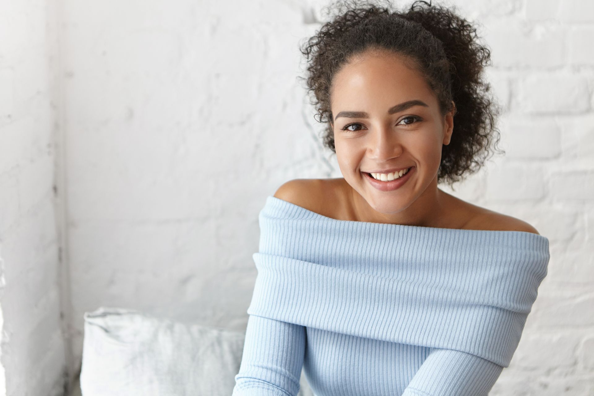 A woman in a blue sweater is smiling while sitting on a couch.