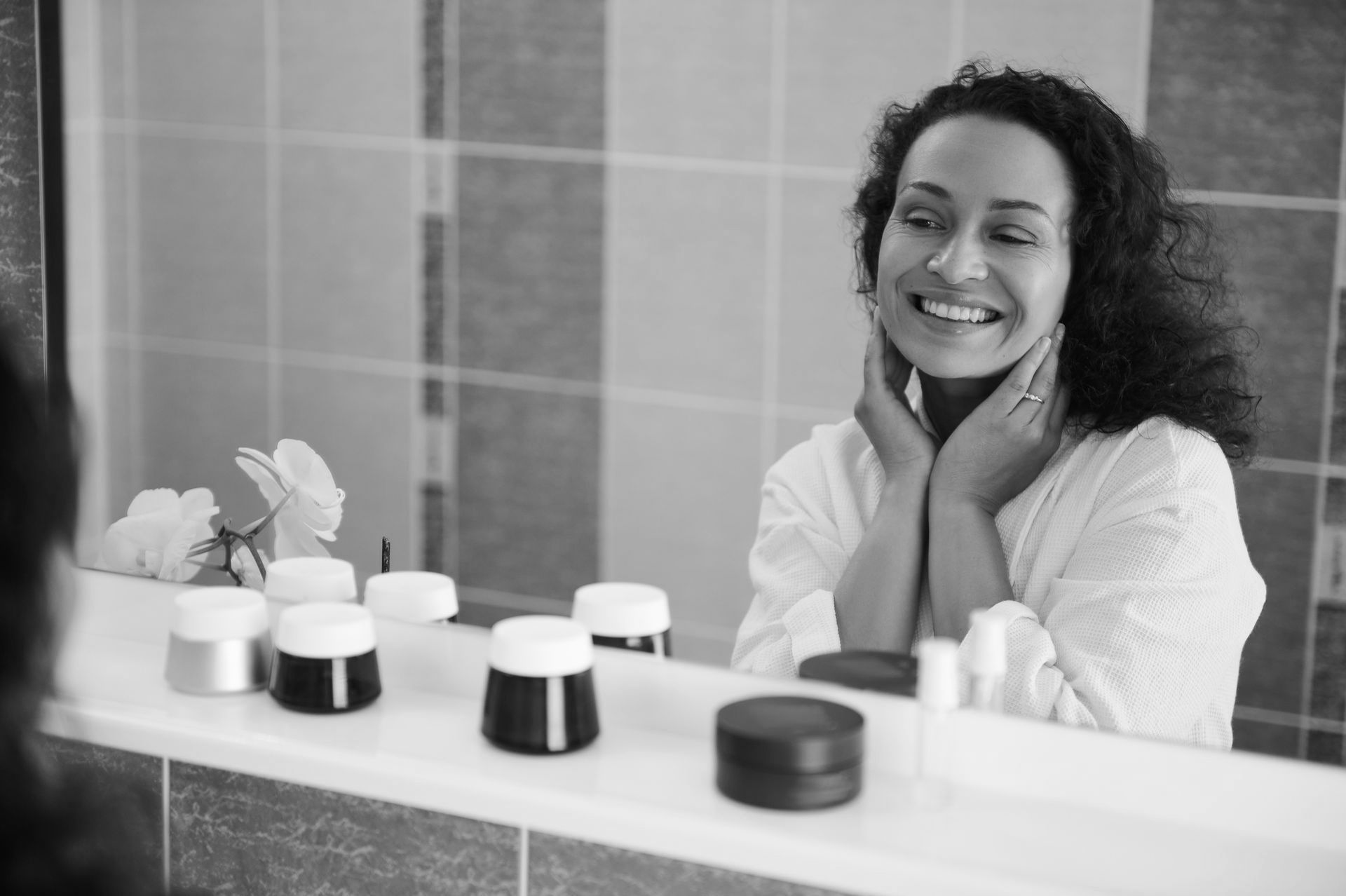 A woman is smiling in front of a mirror in a bathroom.