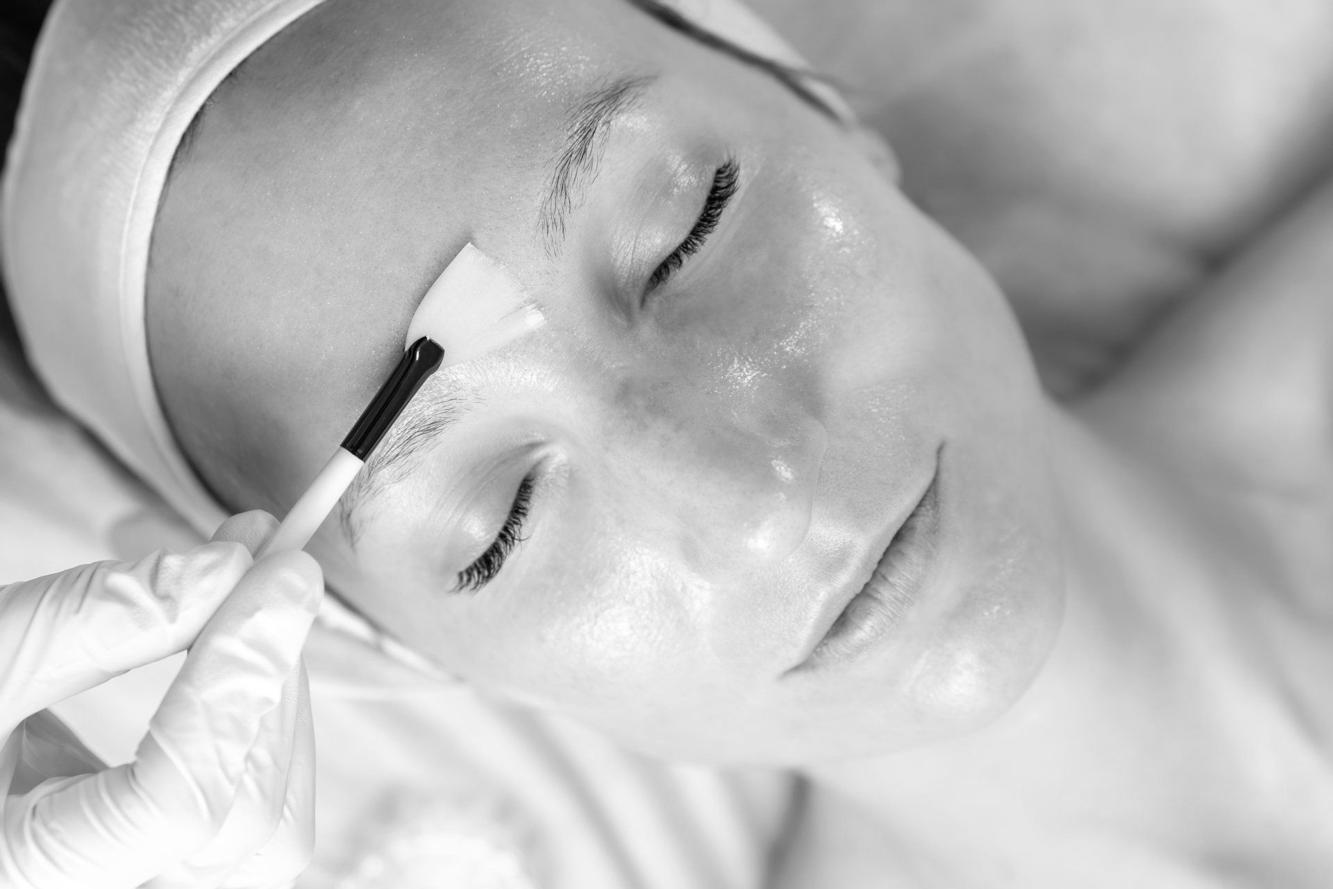 A woman is getting a facial treatment in a black and white photo.