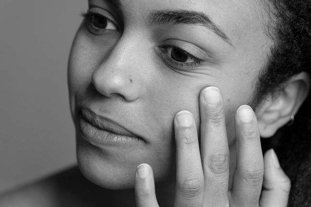 A woman is touching her face with her hand in a black and white photo.