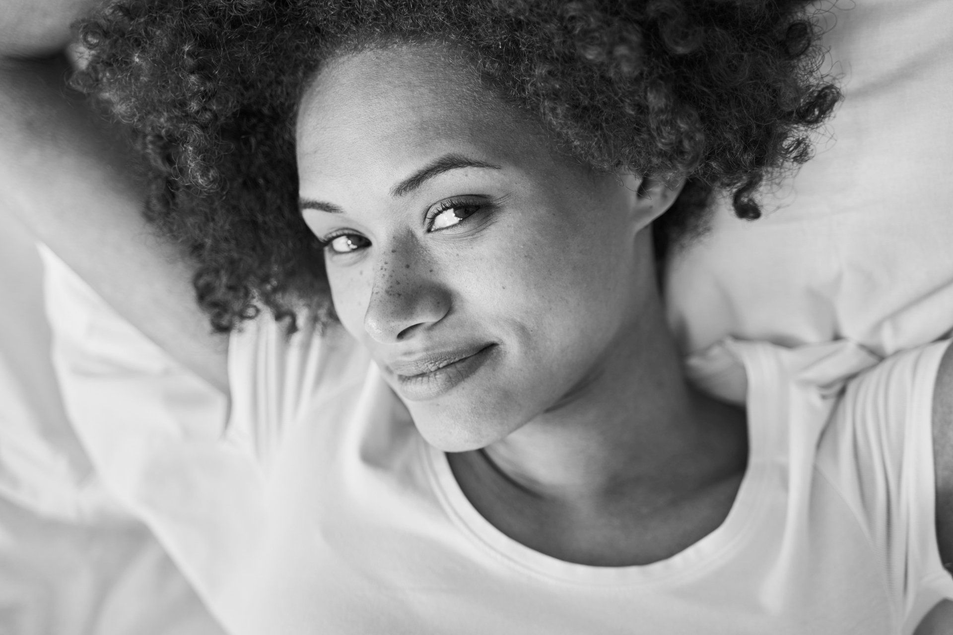 A black and white photo of a woman laying on a bed with her arms outstretched.