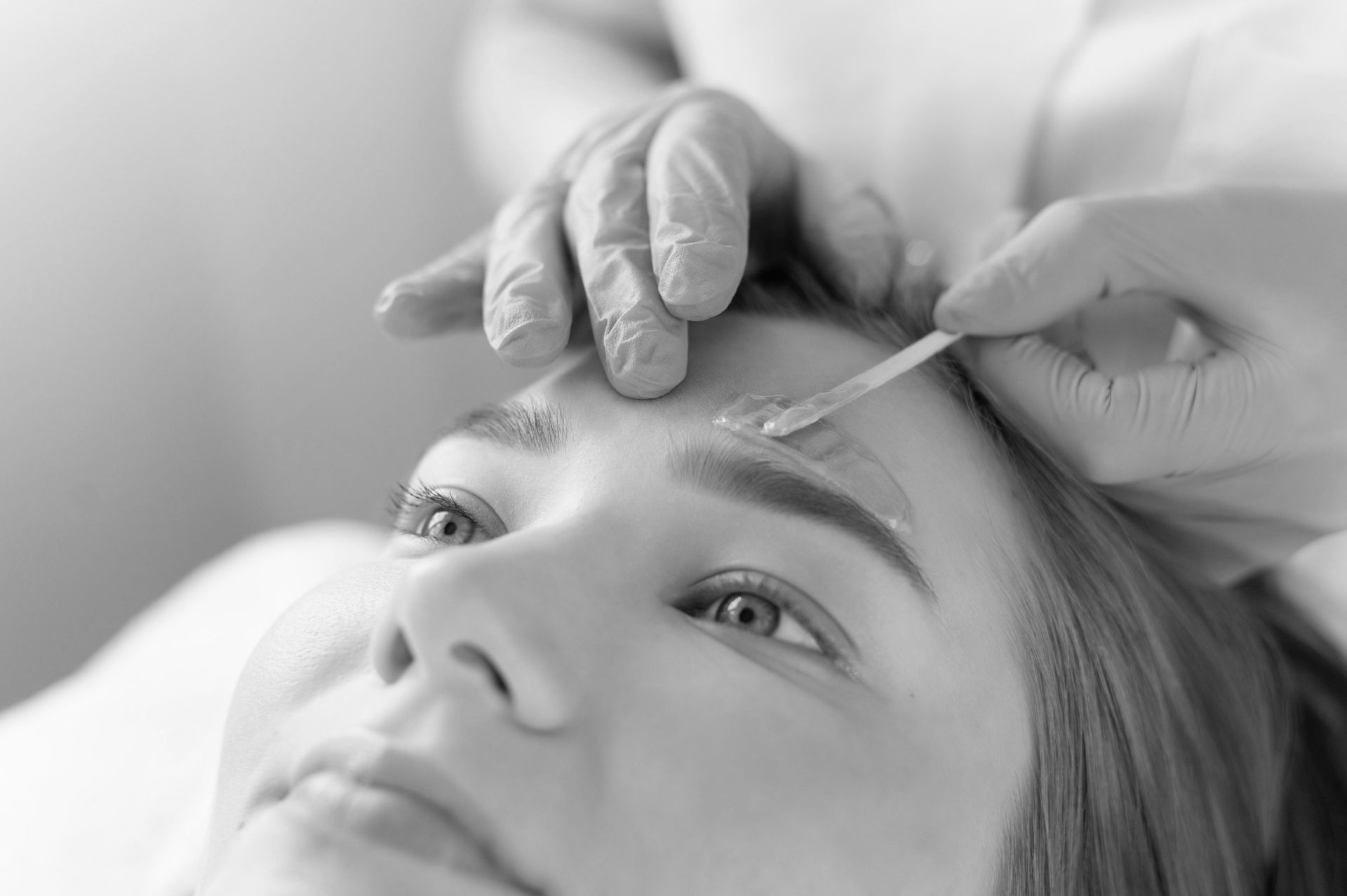 A woman is getting her eyebrows waxed in a black and white photo.