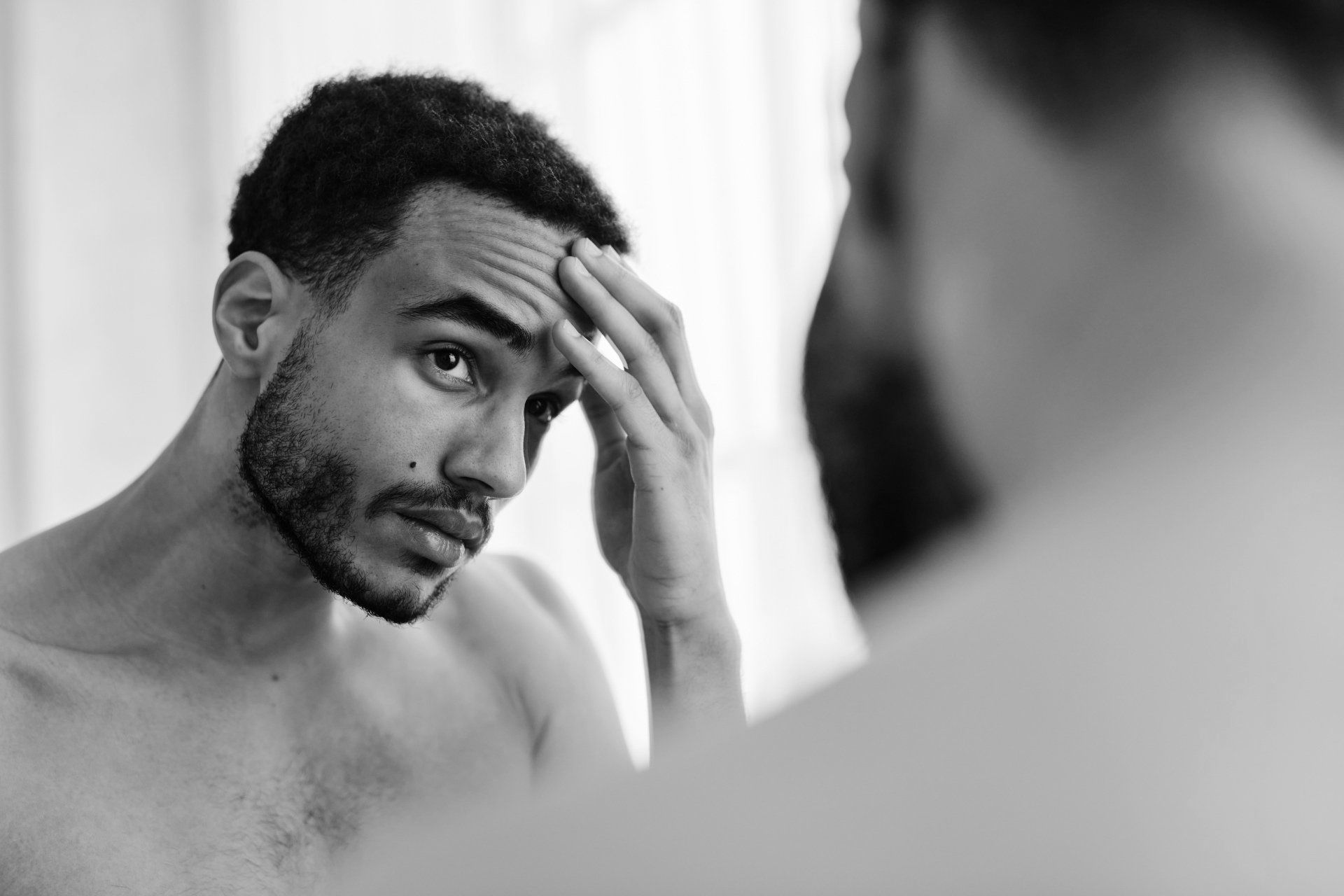 A shirtless man is looking at his face in a mirror.