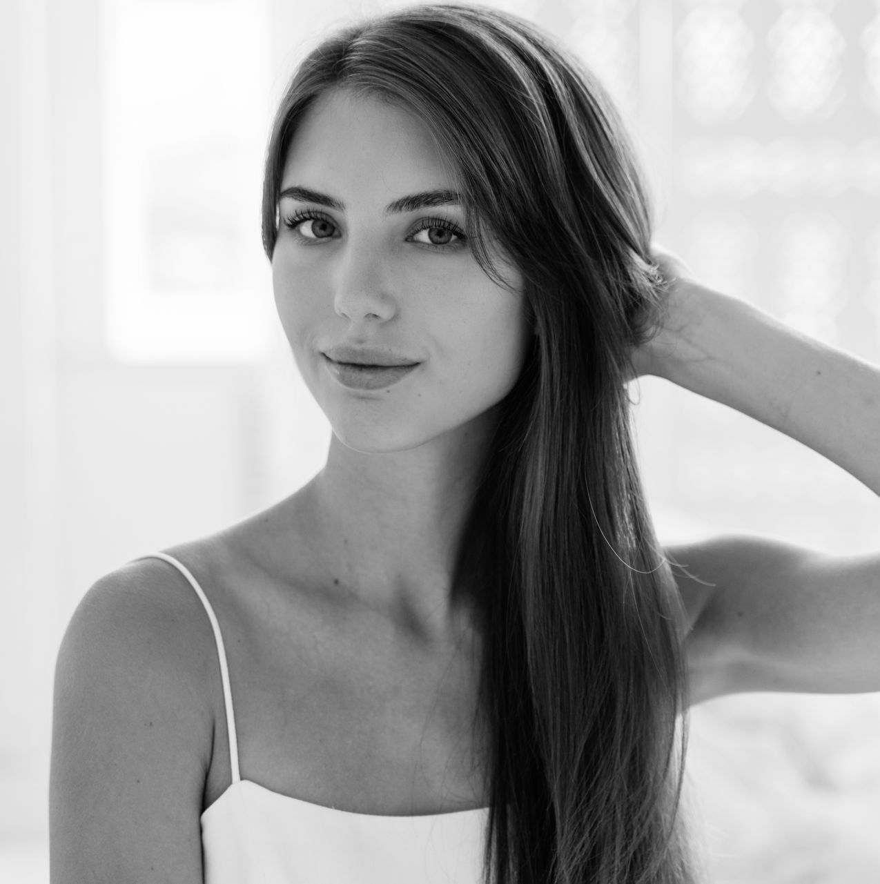 A black and white photo of a woman with long hair in a white tank top.