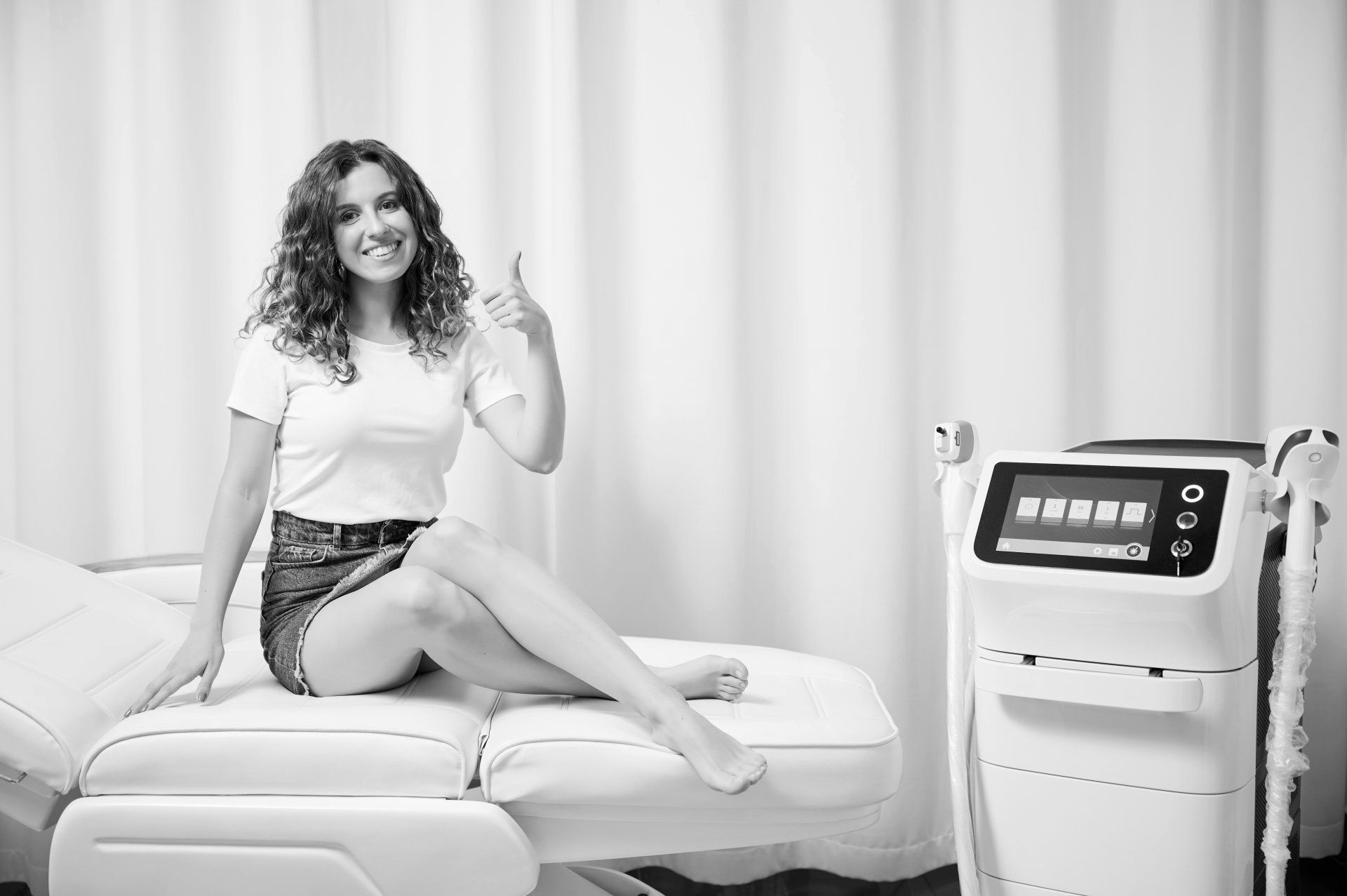 A woman is sitting on a bed next to a machine and giving a thumbs up.