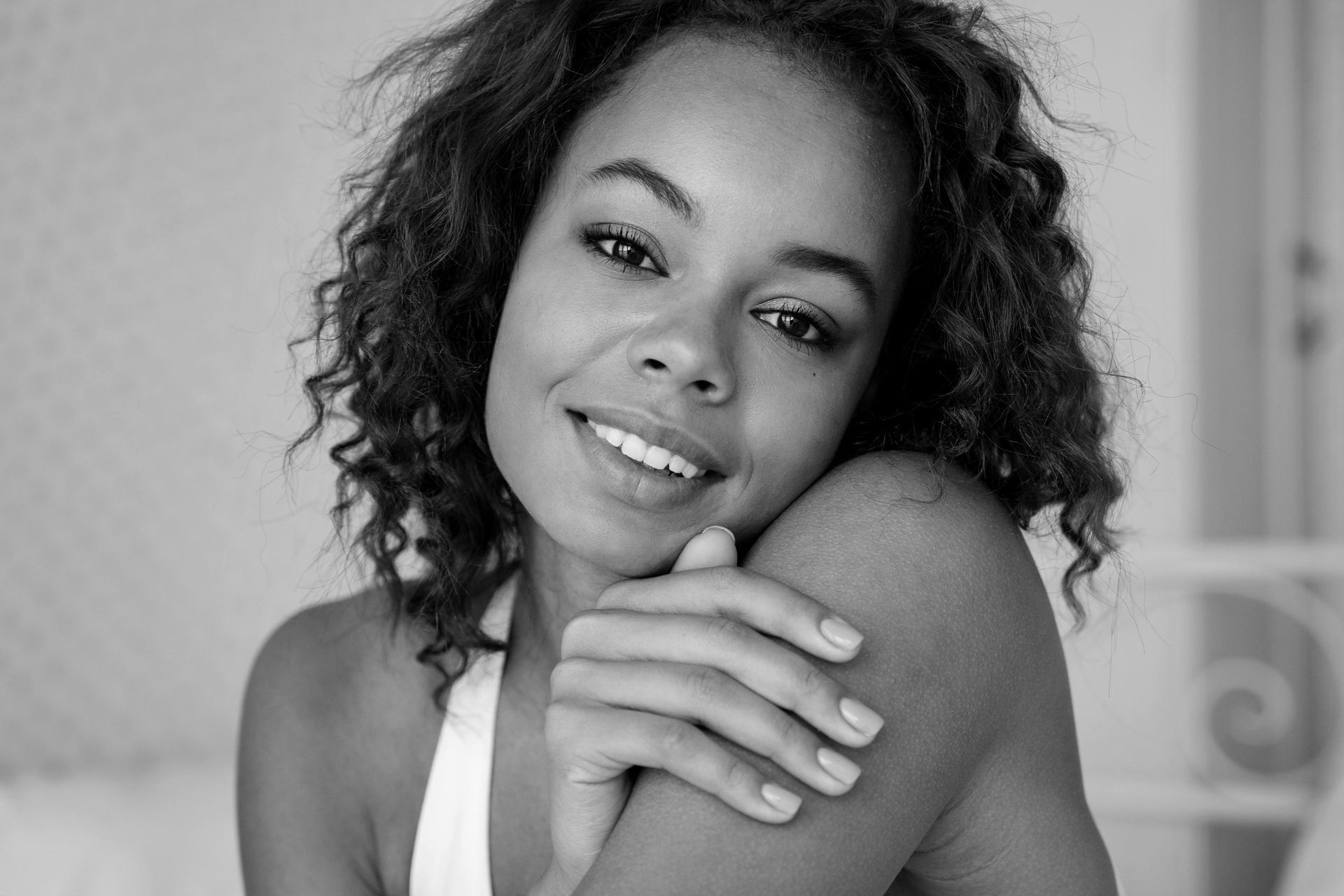 A black and white photo of a woman smiling with her hands on her shoulder.