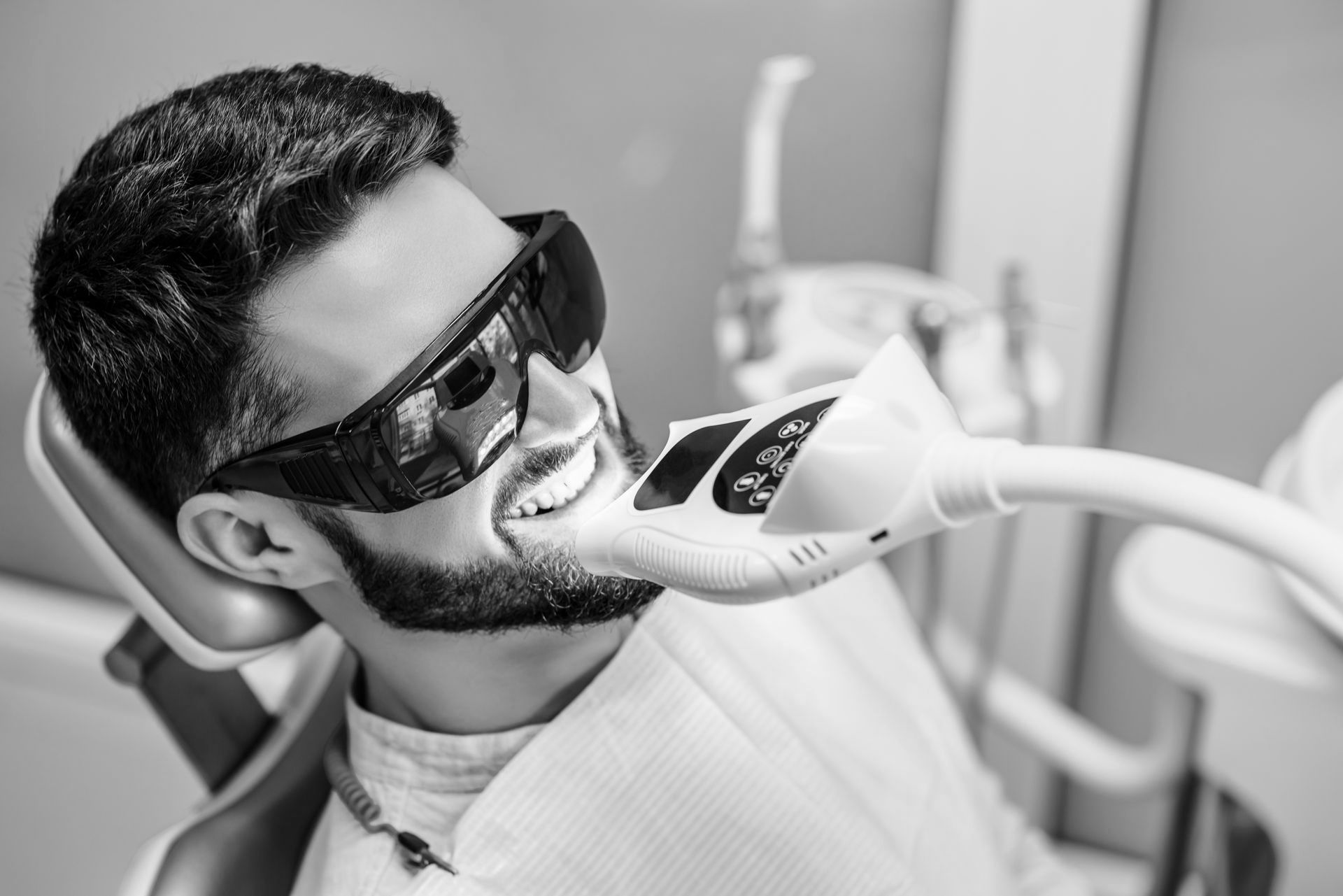 A man is sitting in a dental chair getting his teeth whitened.