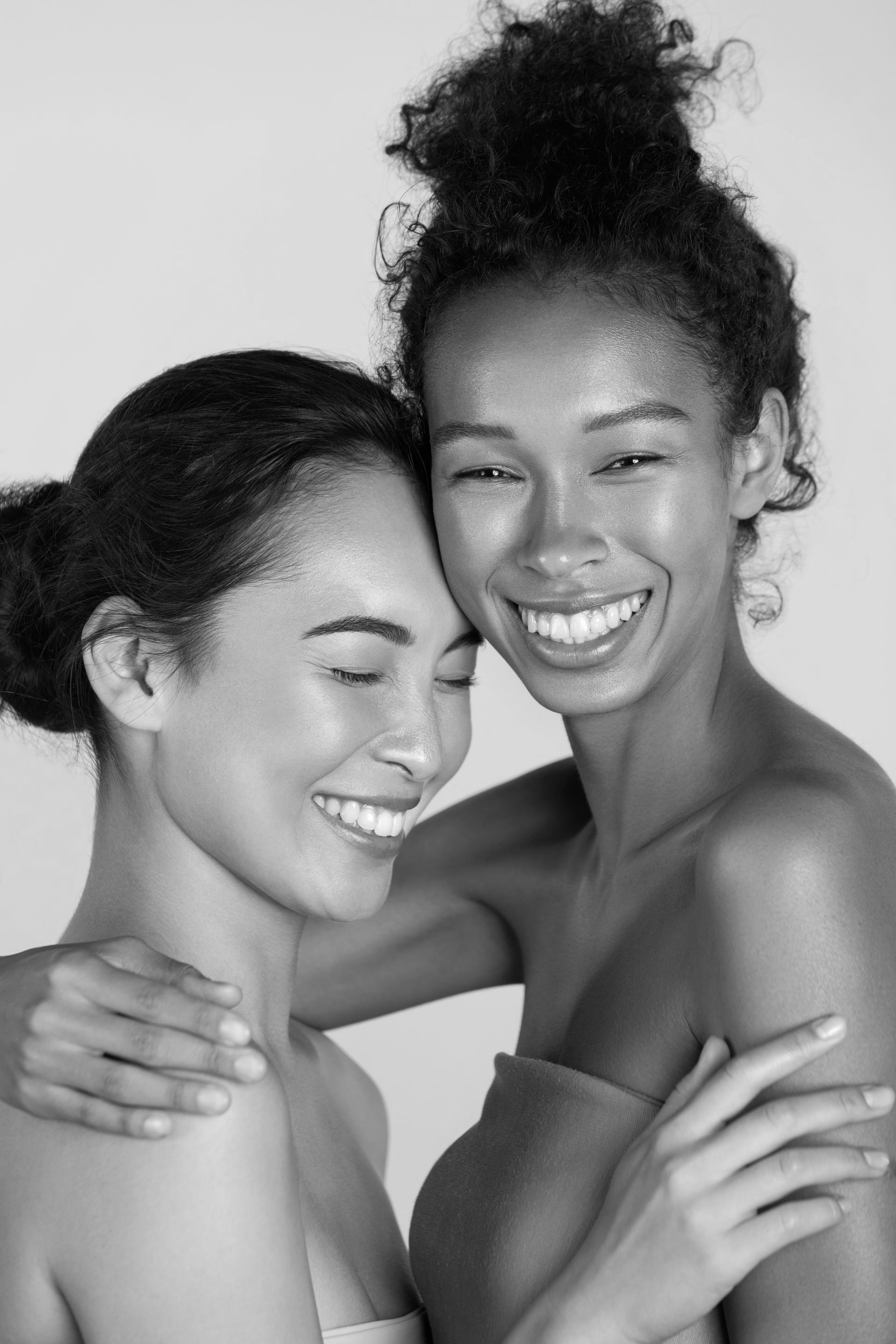 Two women are hugging each other and smiling in a black and white photo.