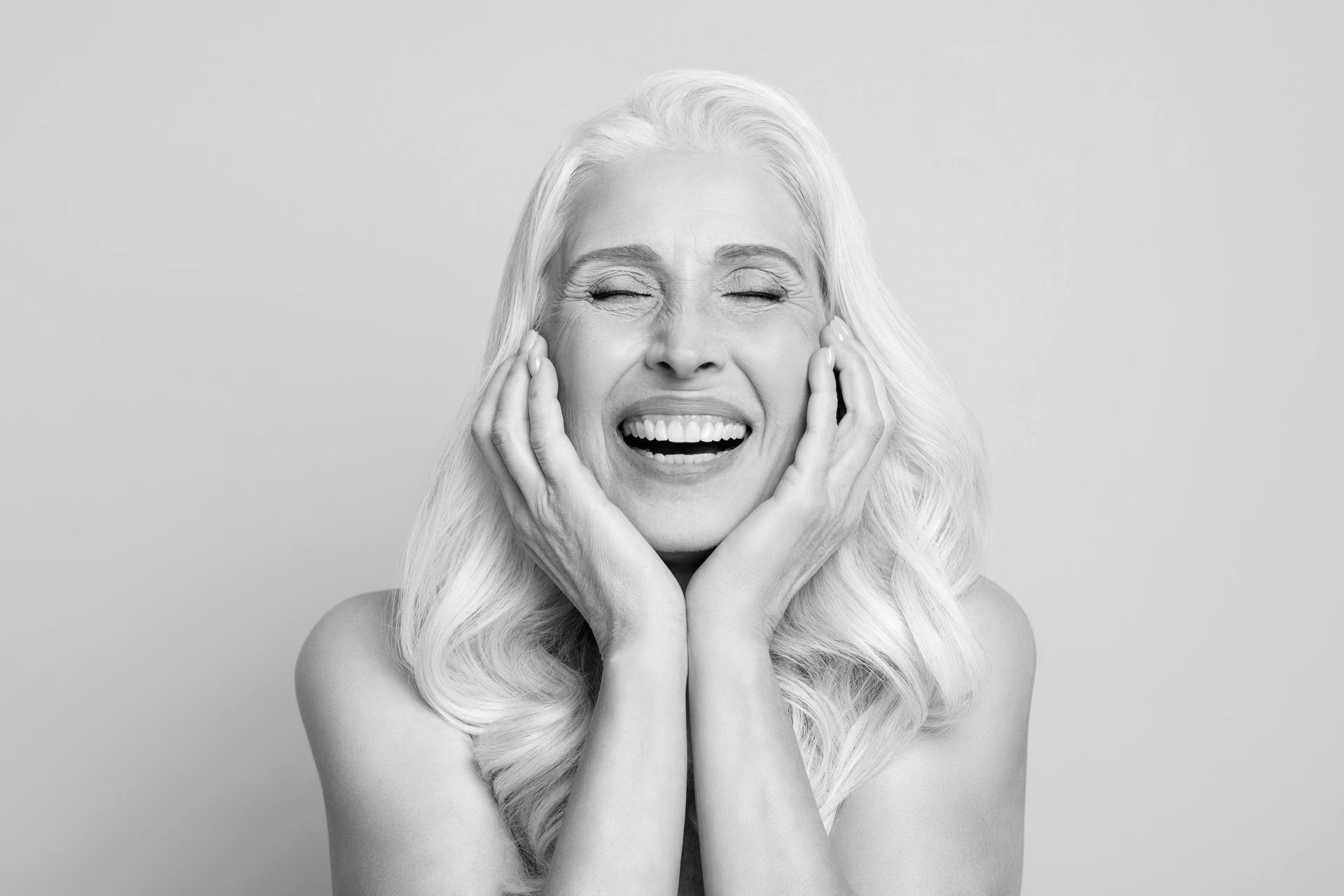 A black and white photo of a woman laughing with her eyes closed.