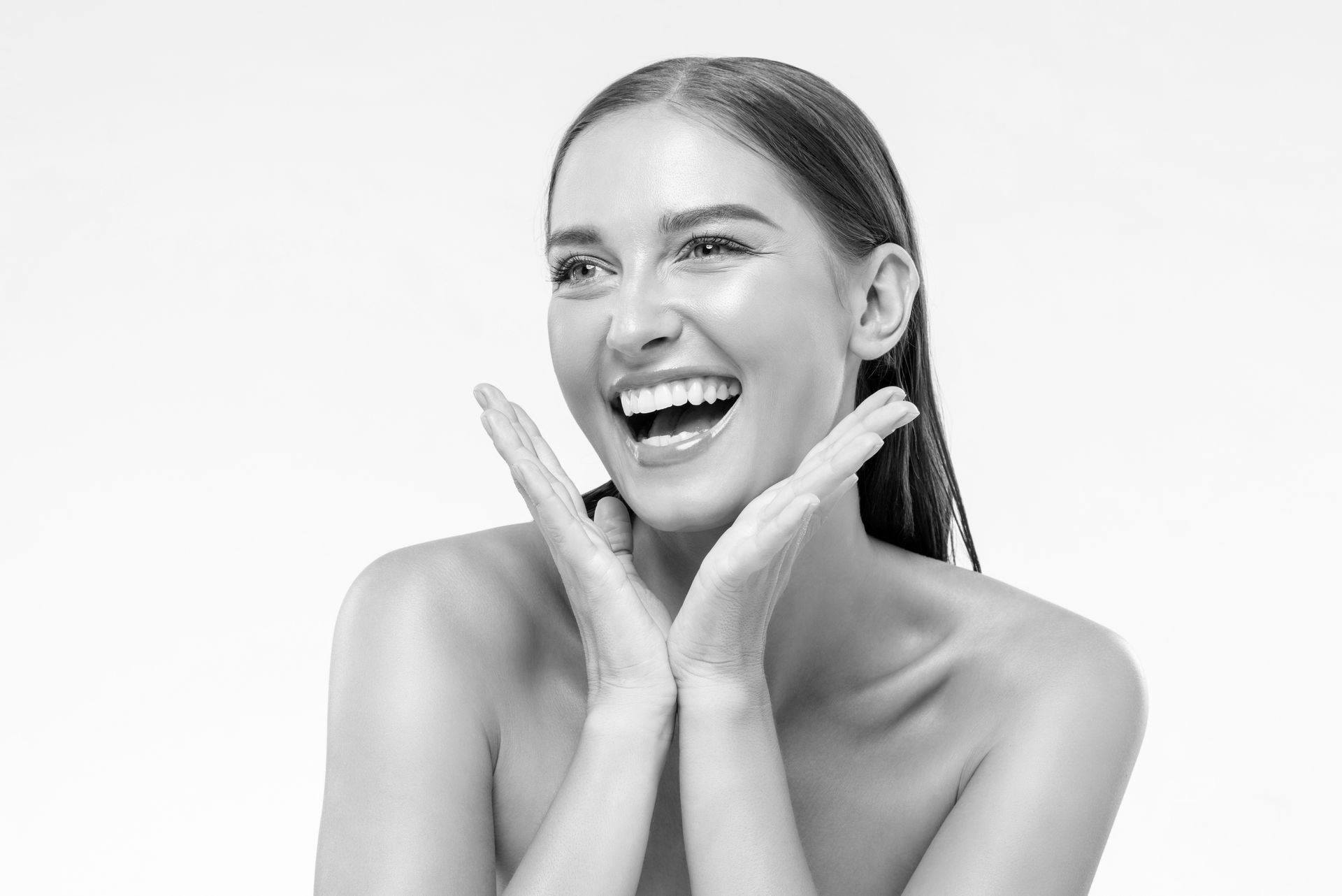 A black and white photo of a woman laughing with her hands on her face.