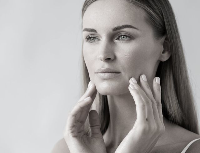 A woman is touching her face in a black and white photo.