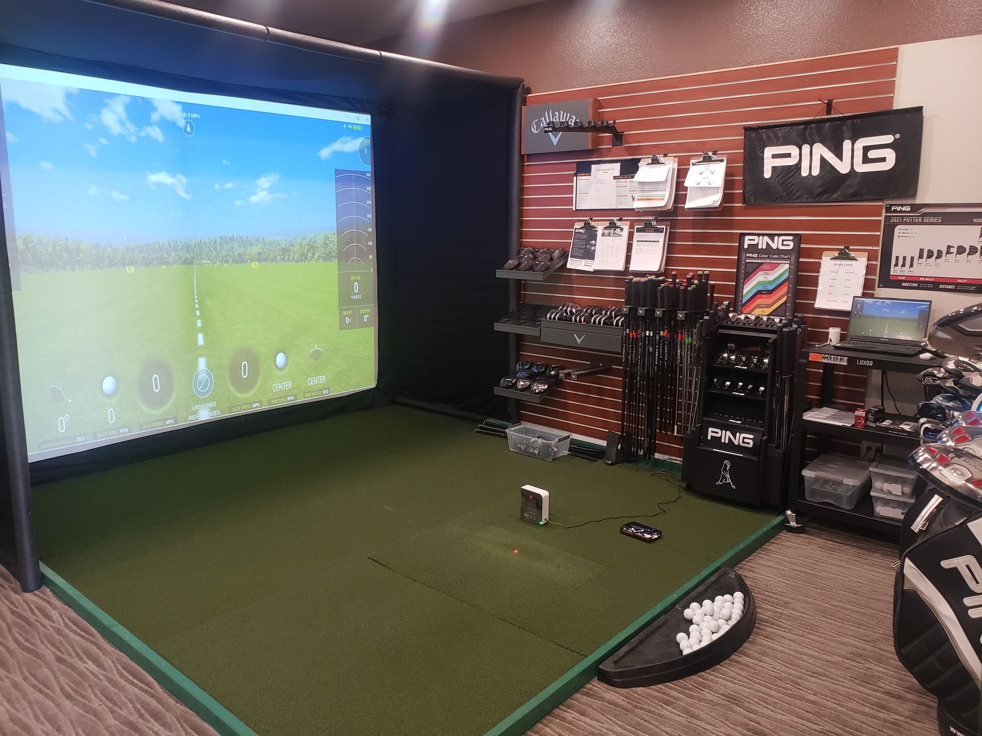 A golf simulator with a ping sign on the wall.