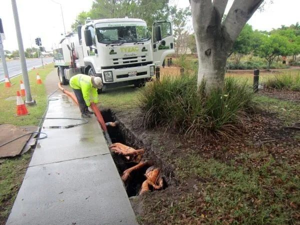 A Worker in a High-vis Vest Reaches Into a Dark Ditch Beside a Truck — Tyzac Group in Beerwah, QLD