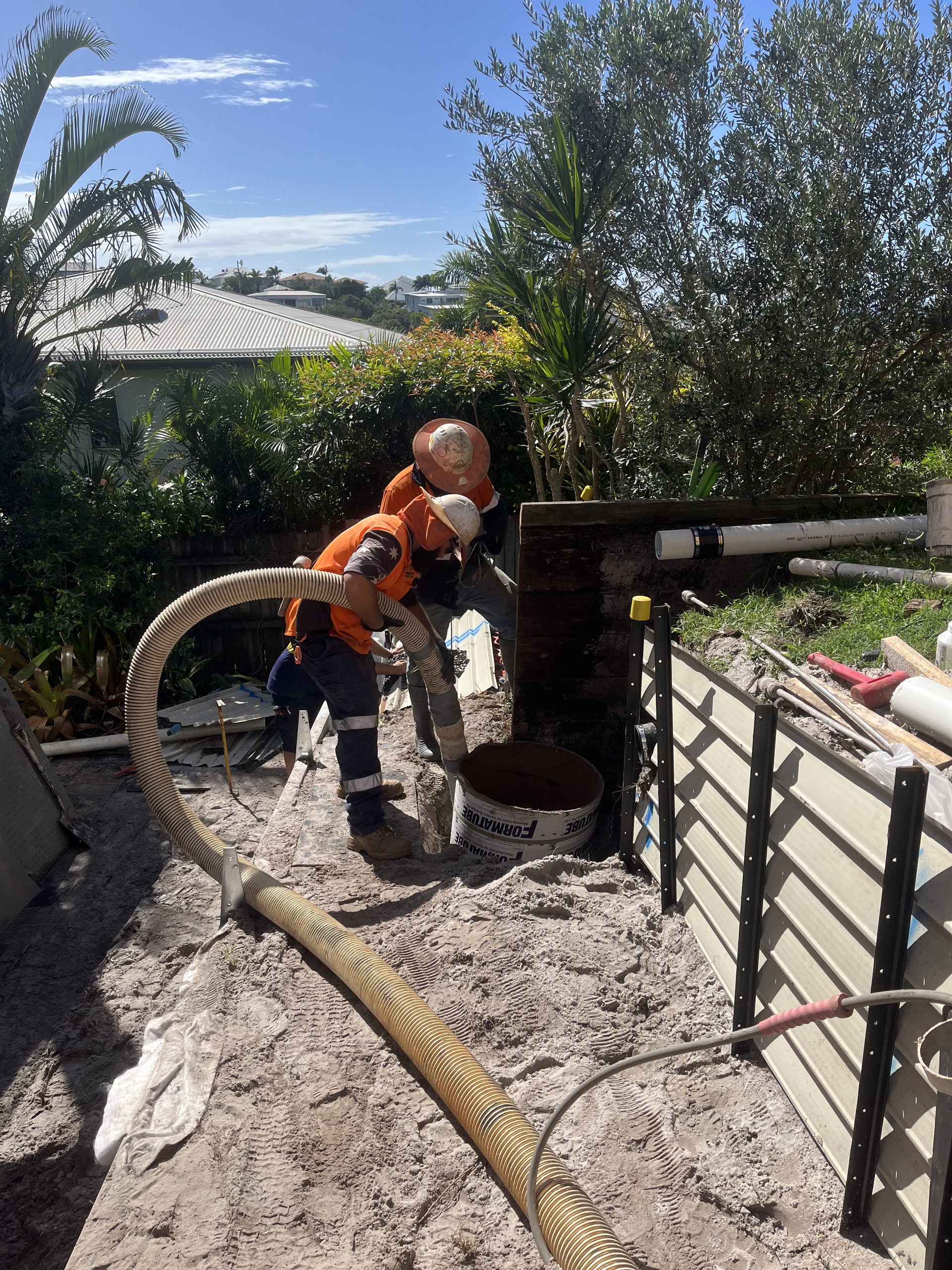 Two Workers in Orange Vests Use a Pump Hose to Fill a Bucket — Tyzac Group in Beerwah, QLD