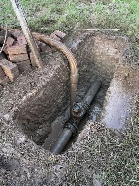 A Pipe Joint Exposed in a Dirt Pit, With a Hose Extending From It and Bricks Visible — Tyzac Group in Beerwah, QLD