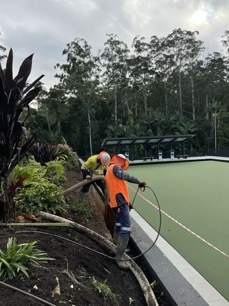 Two Workers Installing Wiring Near a Green Sports Field With Trees in the Background — Tyzac Group in Beerwah, QLD