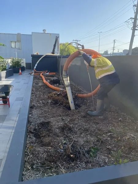Worker in Safety Vest Installs Drainage Pipe in a Planter Box — Tyzac Group in Beerwah, QLD