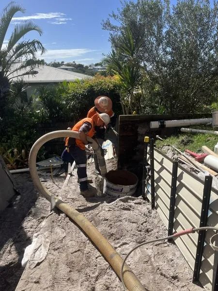 Two Workers in Safety Gear Using a Hose to Fill a Hole in a Yard With Material — Tyzac Group in Beerwah, QLD
