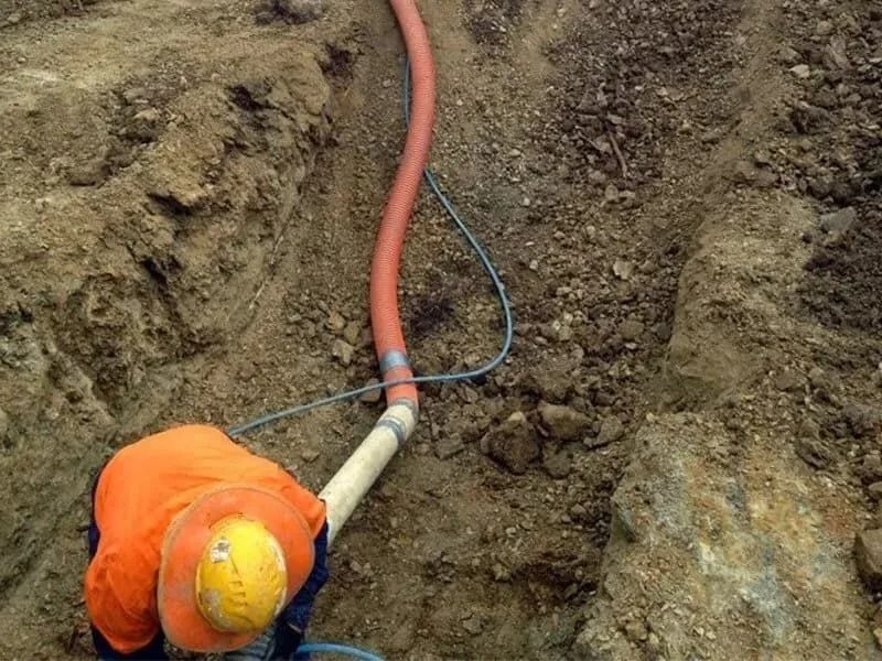 Person in Orange Vest and Hard Hat Working in a Trench With Pipes — Tyzac Group in Beerwah, QLD